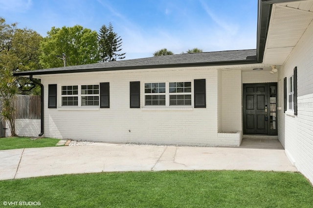 view of front of house with brick siding, roof with shingles, a patio, and fence