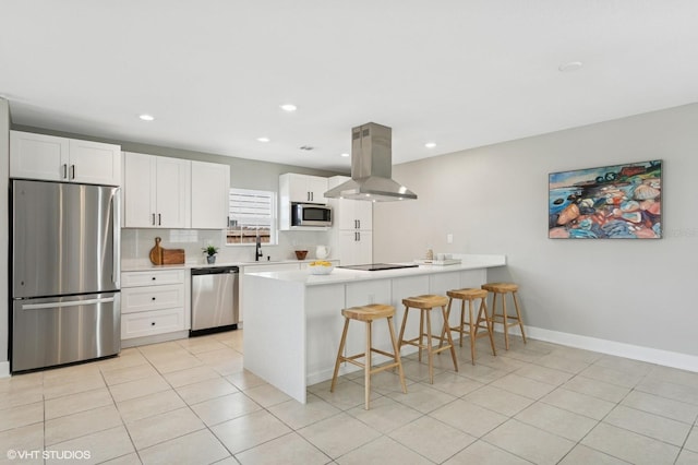 kitchen with a breakfast bar area, a peninsula, island exhaust hood, stainless steel appliances, and white cabinets