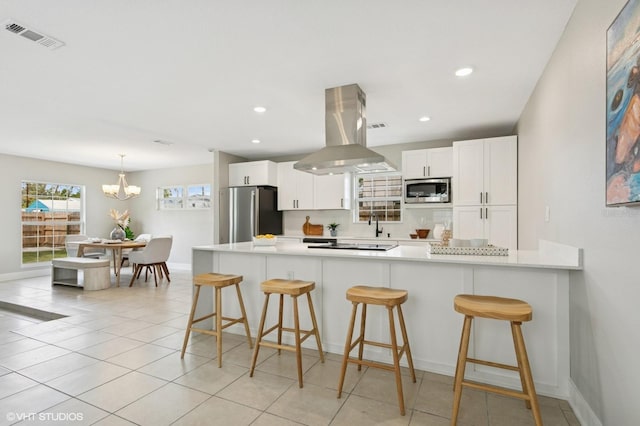 kitchen with visible vents, a peninsula, island exhaust hood, stainless steel appliances, and white cabinetry