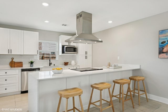 kitchen with visible vents, a peninsula, island exhaust hood, stainless steel appliances, and a sink