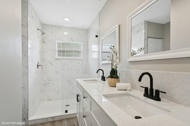 full bathroom featuring double vanity, tiled shower, and a sink