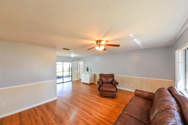 living area featuring visible vents, baseboards, ceiling fan, and wood finished floors