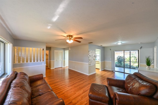 living room featuring a ceiling fan, baseboards, visible vents, light wood-style floors, and a textured ceiling