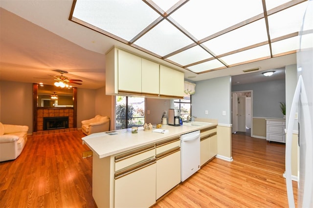 kitchen featuring ceiling fan, light countertops, light wood-type flooring, a tile fireplace, and white appliances