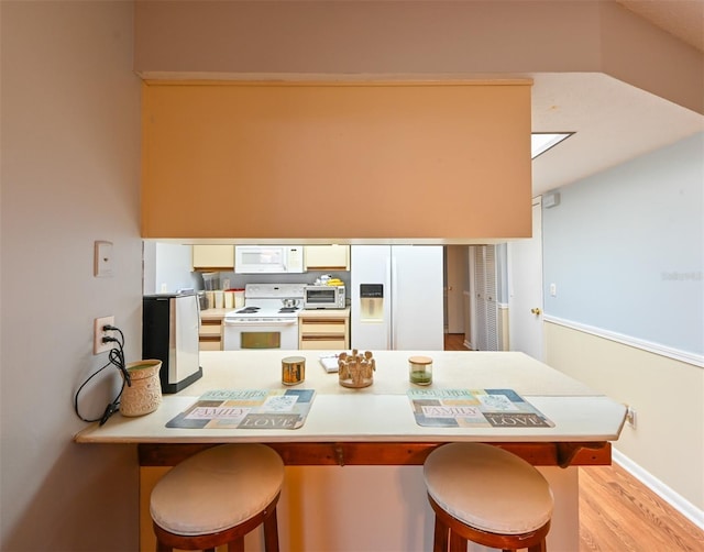 kitchen featuring white cabinetry, white appliances, a breakfast bar area, and a peninsula