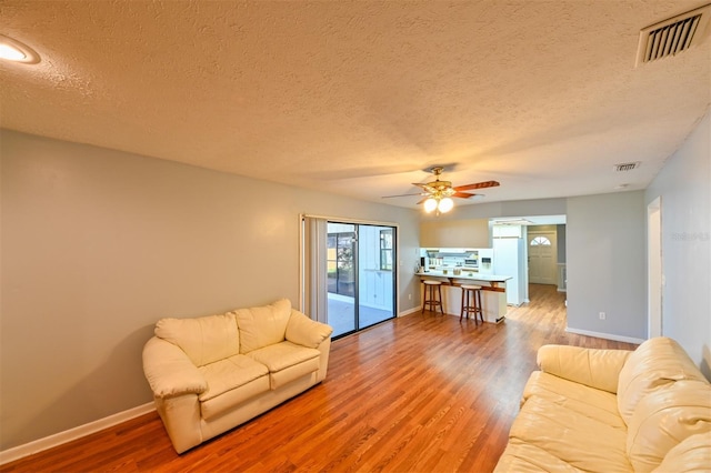 living room featuring baseboards, wood finished floors, visible vents, and ceiling fan