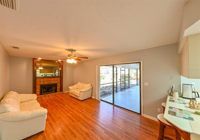 living room with light wood-type flooring, visible vents, baseboards, ceiling fan, and a tile fireplace