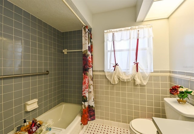 full bath featuring shower / bath combination with curtain, a wainscoted wall, toilet, and tile walls