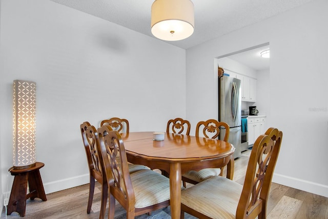 dining space with light wood finished floors, a textured ceiling, and baseboards