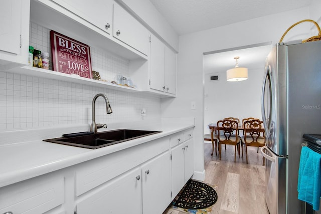 kitchen featuring backsplash, light countertops, light wood-style flooring, white cabinets, and a sink