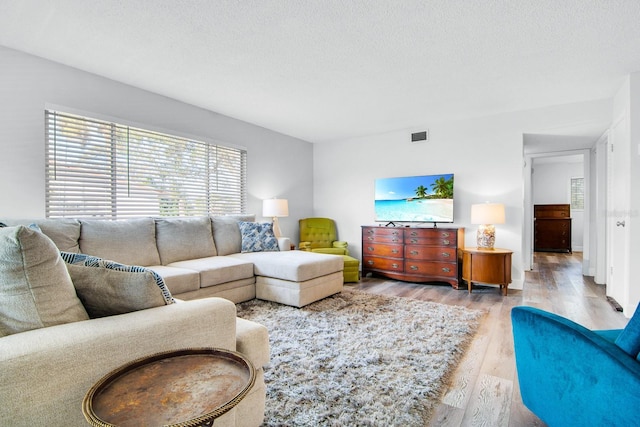 living area with visible vents, a textured ceiling, and wood finished floors