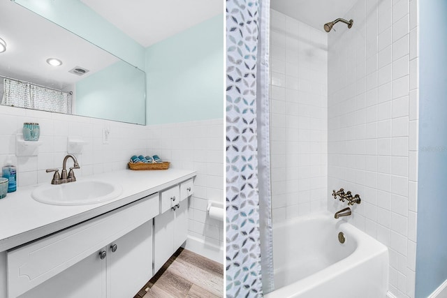 bathroom with visible vents, wood finished floors, tile walls, shower / tub combo, and vanity