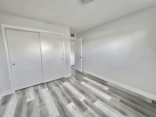 unfurnished bedroom with wood finished floors, baseboards, visible vents, a closet, and a textured ceiling