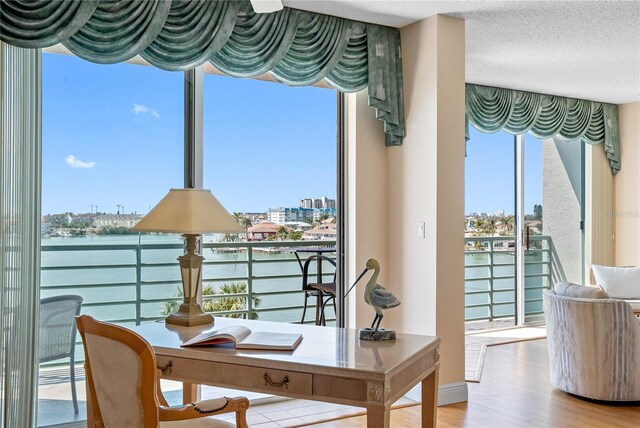 interior space featuring a wealth of natural light, a water view, a textured ceiling, and wood finished floors