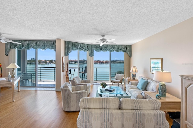 living area with wood finished floors, a ceiling fan, a water view, and a textured ceiling