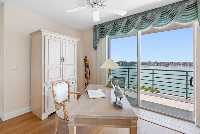 home office with wood finished floors, a ceiling fan, a fireplace, a water view, and a textured ceiling