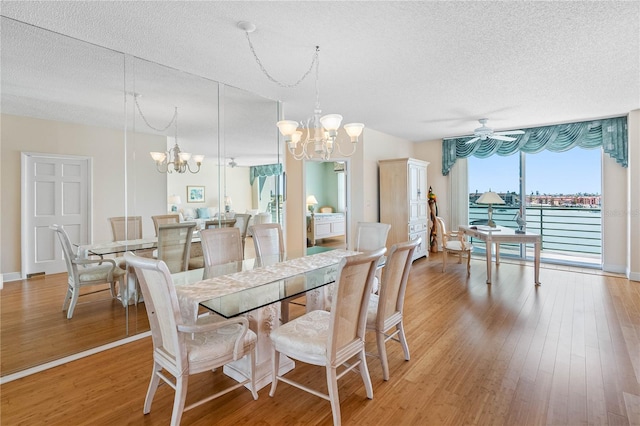 dining room with ceiling fan with notable chandelier, a textured ceiling, and light wood-type flooring