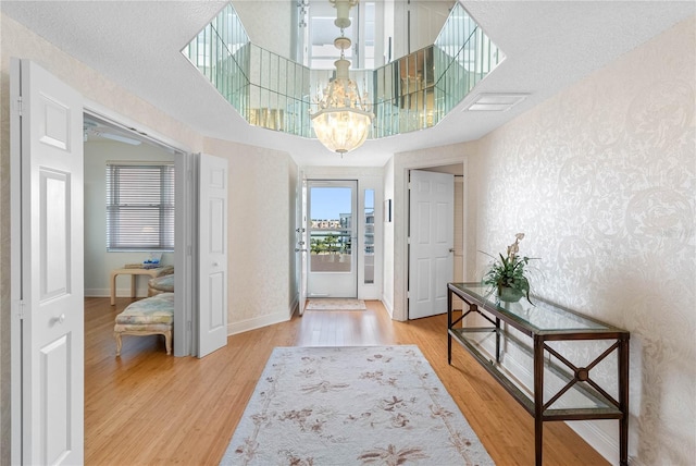 entryway featuring wallpapered walls, baseboards, light wood-style flooring, a high ceiling, and a notable chandelier