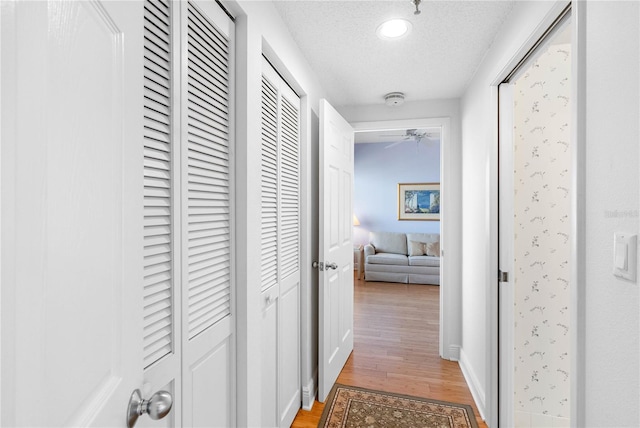 hall featuring baseboards, a textured ceiling, and light wood-style floors