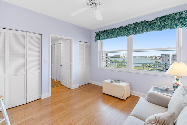 living area with baseboards, light wood-type flooring, ceiling fan, and a water view