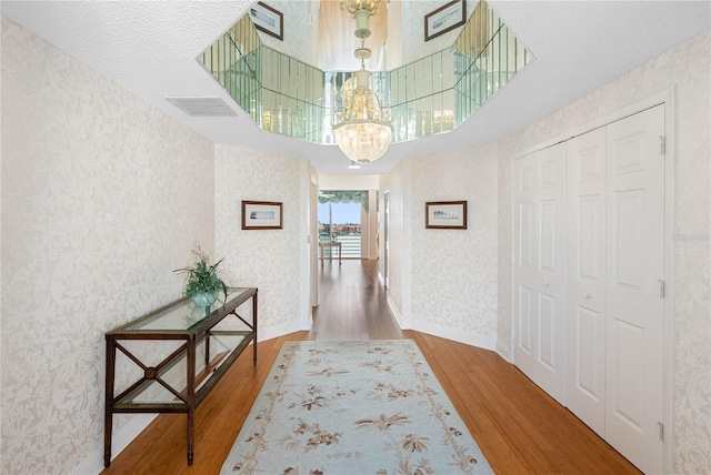 hallway with wallpapered walls, a notable chandelier, wood finished floors, and baseboards