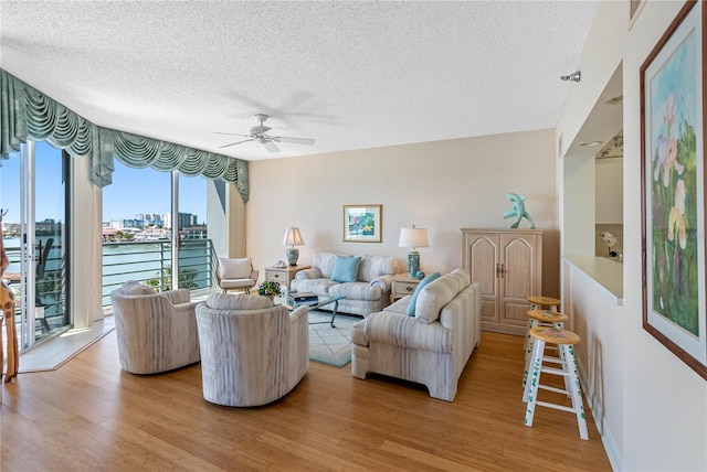 living room with a view of city, light wood-style floors, a ceiling fan, and a textured ceiling