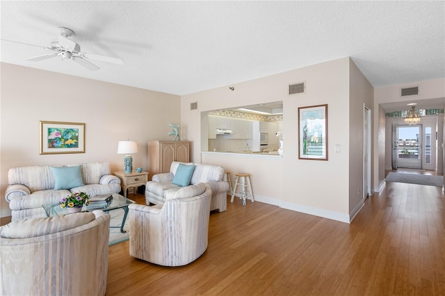 living area with visible vents, baseboards, a textured ceiling, a ceiling fan, and wood-type flooring