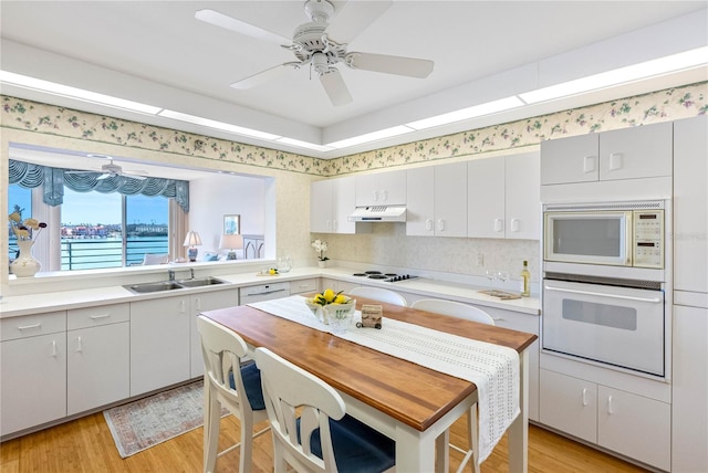 kitchen with under cabinet range hood, white appliances, light countertops, and a sink