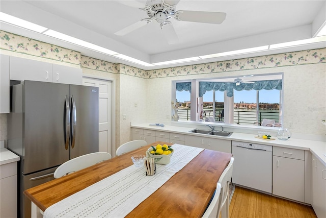 kitchen with a sink, wallpapered walls, dishwasher, and freestanding refrigerator