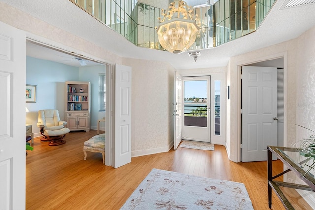 entryway featuring wood finished floors, visible vents, baseboards, a towering ceiling, and a chandelier