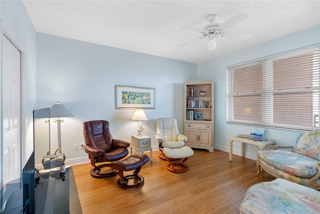 living area featuring ceiling fan, baseboards, and wood finished floors