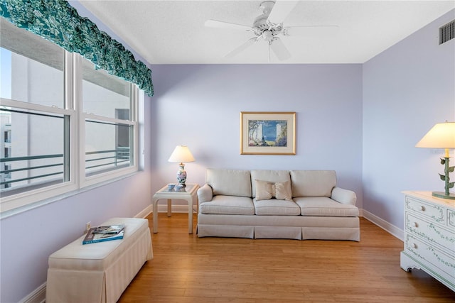 living room with light wood finished floors, visible vents, baseboards, and ceiling fan