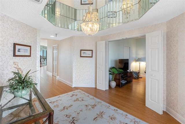 hallway with wallpapered walls, baseboards, a chandelier, a towering ceiling, and wood finished floors