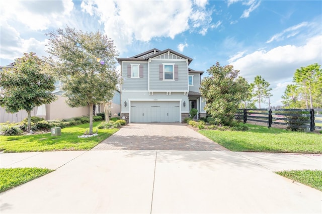 craftsman house with a front yard, fence, a garage, stone siding, and decorative driveway