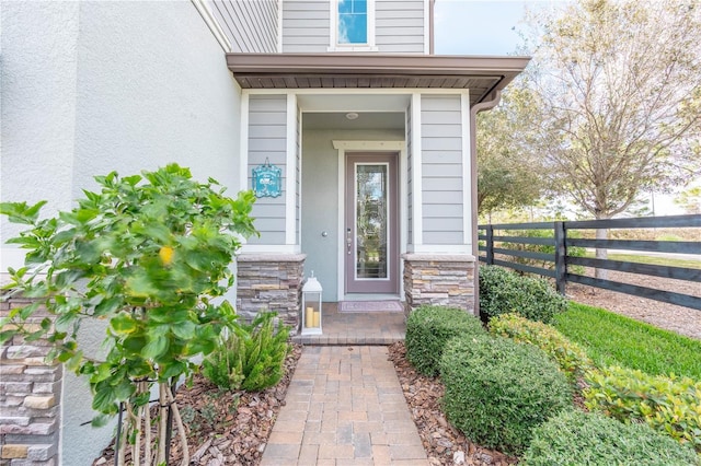 entrance to property with stone siding, stucco siding, and fence