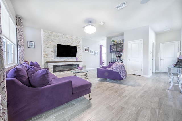 living area with a stone fireplace, light wood-style flooring, baseboards, and visible vents