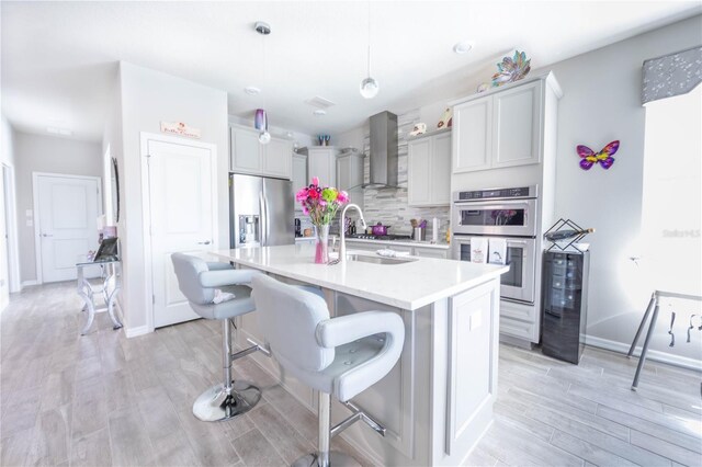 kitchen with light wood-style flooring, appliances with stainless steel finishes, wall chimney exhaust hood, and a sink