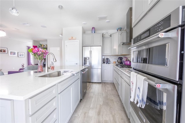 kitchen featuring a sink, decorative backsplash, light wood-style floors, appliances with stainless steel finishes, and wall chimney exhaust hood