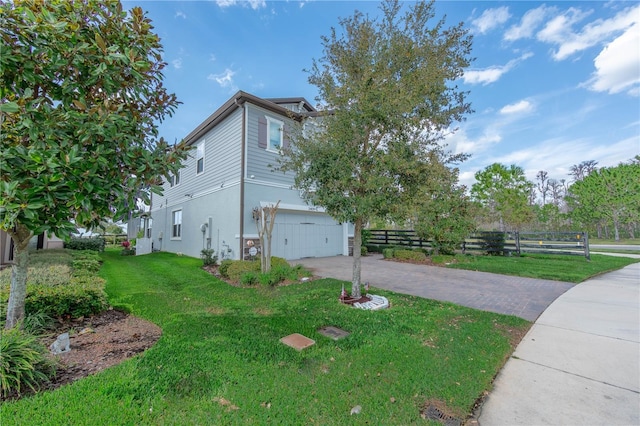 view of side of property featuring fence, a garage, a lawn, stucco siding, and driveway