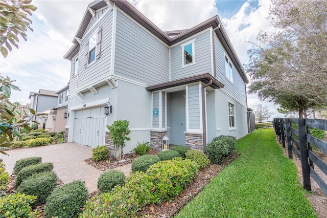 view of side of home featuring stucco siding, fence, stone siding, driveway, and a garage