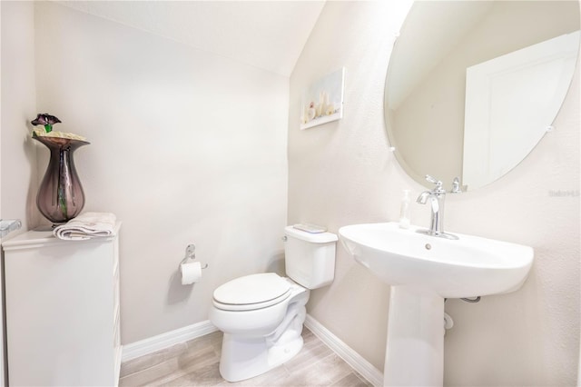 half bath featuring toilet, baseboards, vaulted ceiling, and wood finished floors