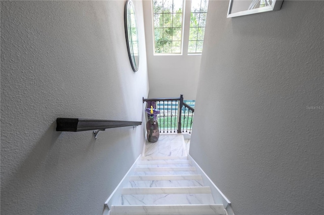 stairway featuring baseboards, marble finish floor, and a textured wall