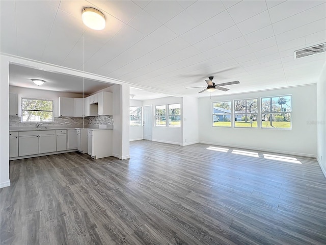 unfurnished living room with a ceiling fan, baseboards, dark wood-style floors, visible vents, and a sink