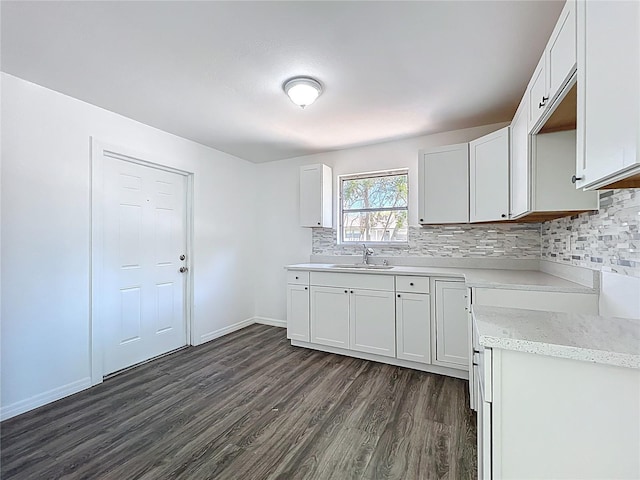 kitchen with a sink, backsplash, dark wood finished floors, white cabinetry, and baseboards