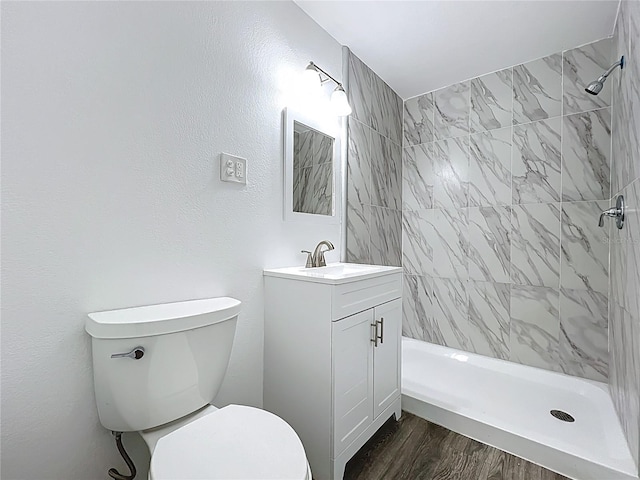 bathroom featuring vanity, toilet, wood finished floors, and a tile shower