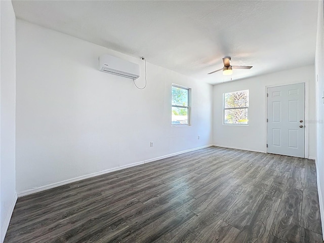 empty room with dark wood finished floors, a ceiling fan, baseboards, and a wall mounted air conditioner