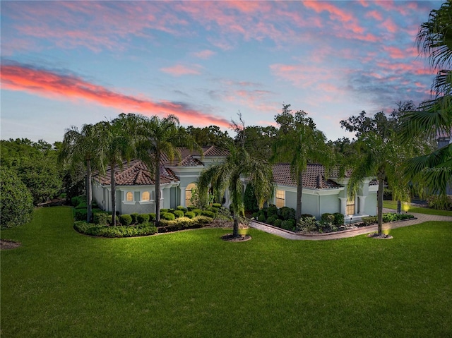 mediterranean / spanish home with a tile roof, stucco siding, and a lawn