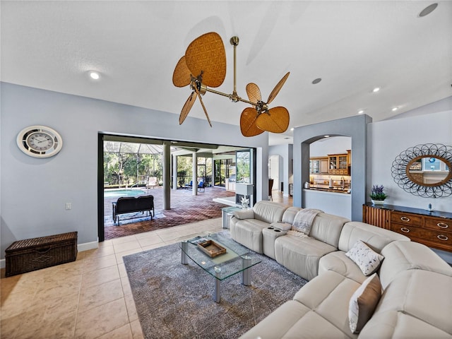 living area with baseboards, a ceiling fan, arched walkways, lofted ceiling, and light tile patterned floors