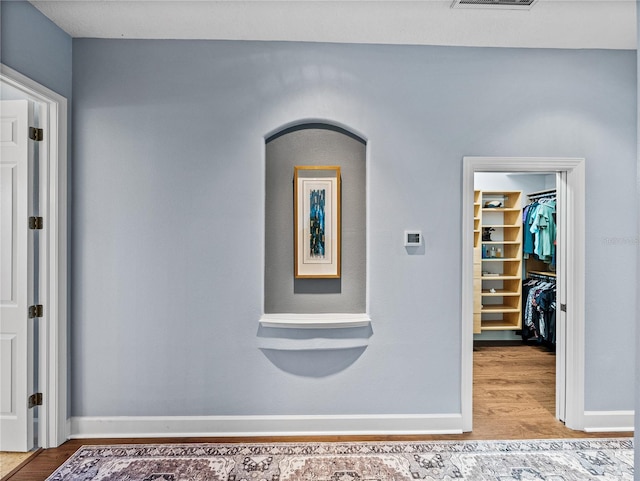 hall featuring baseboards, visible vents, and wood finished floors
