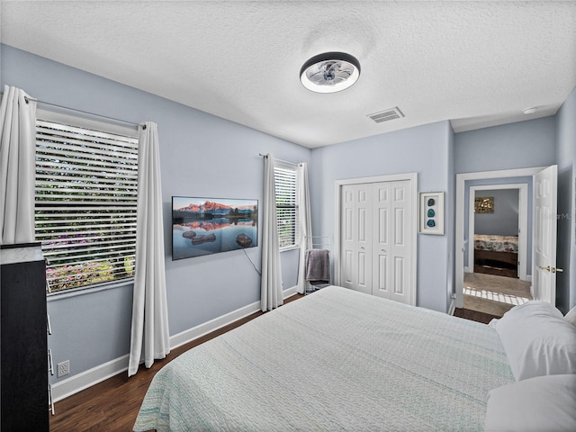 bedroom with baseboards, a textured ceiling, dark wood-style floors, and visible vents